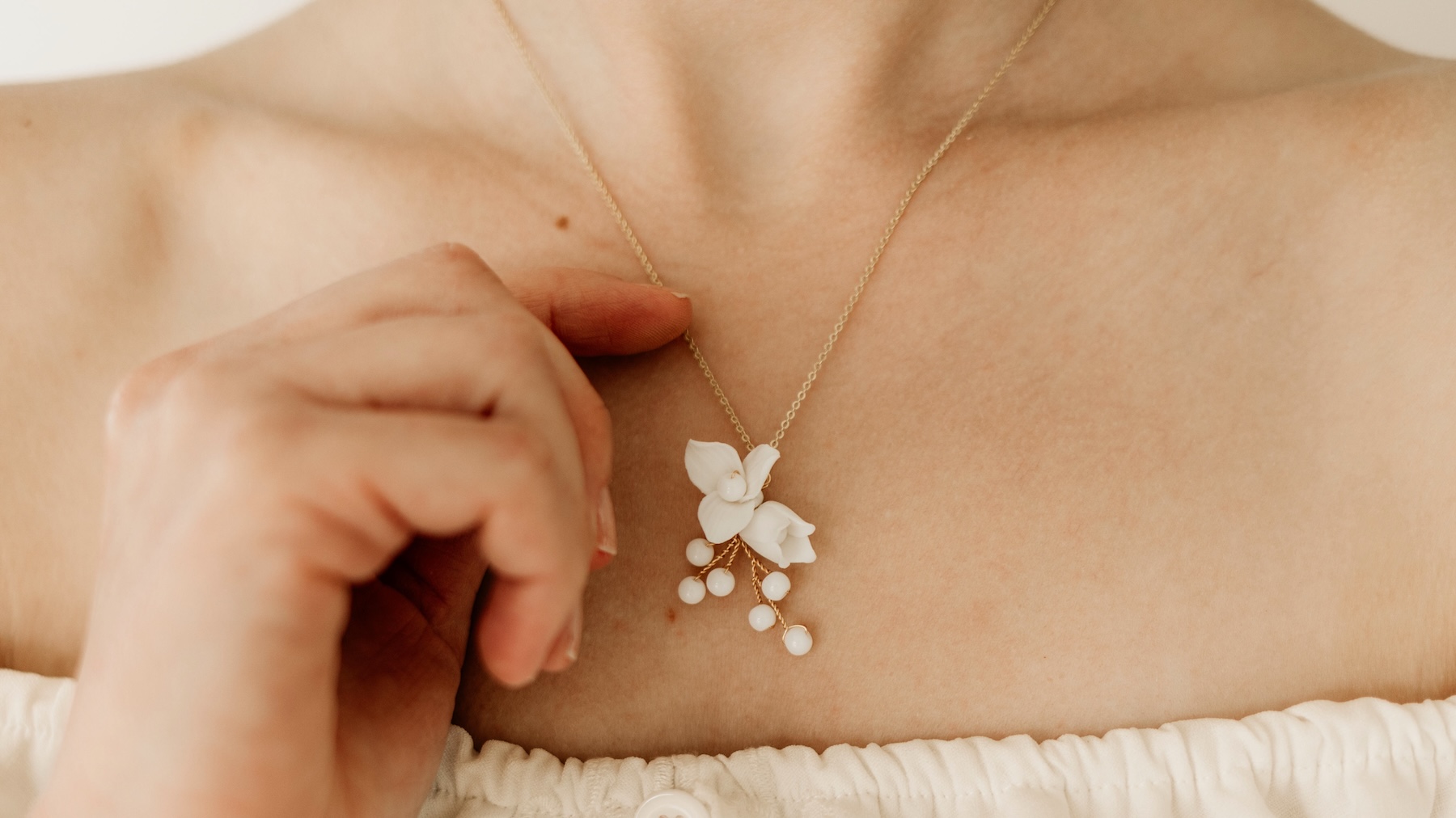 Braut hält Halskette mit Blume und Perlen fest