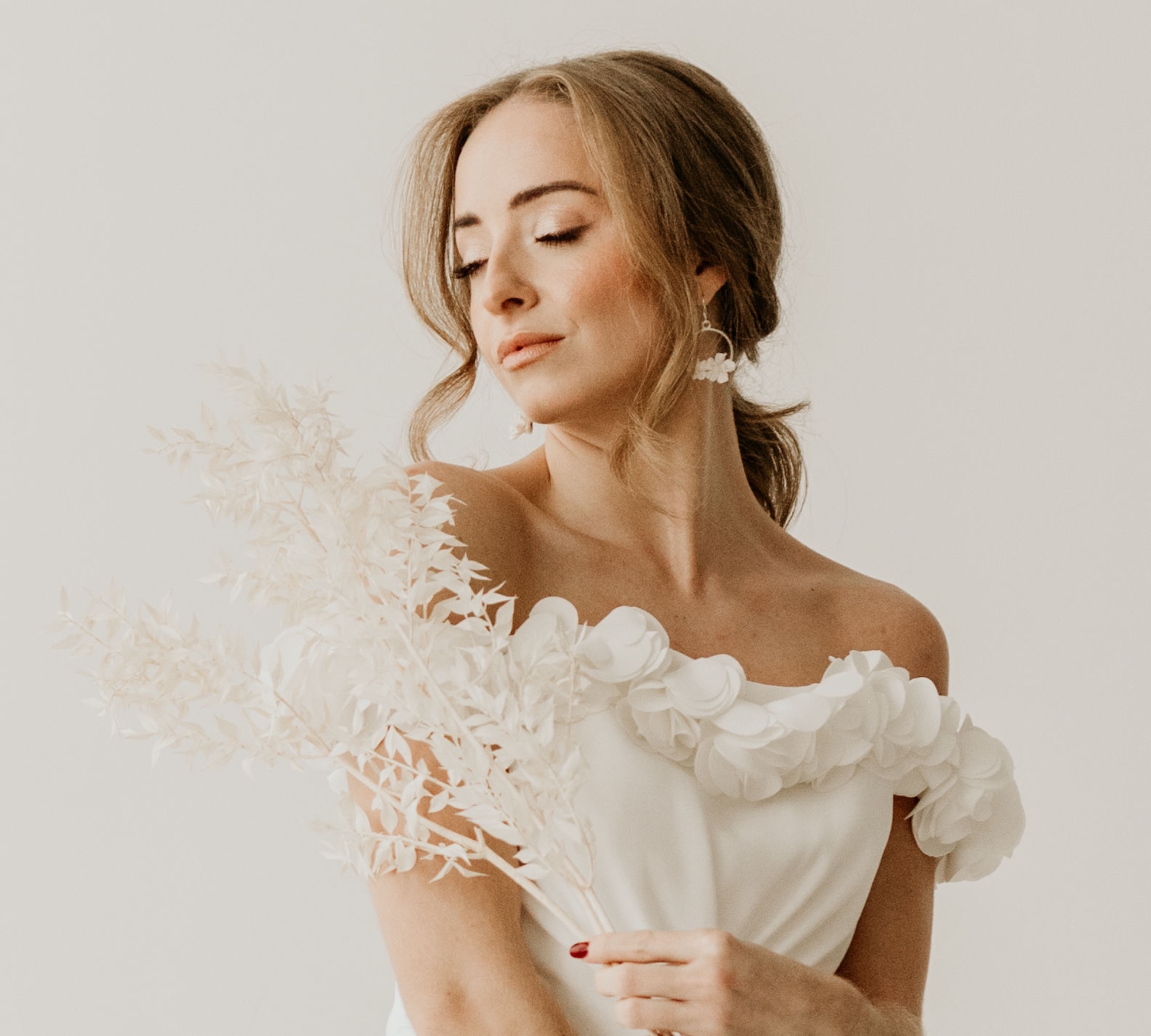 Model mit Brautkleid schaut nach unten, hält Ruscus in der Hand und florale Ohrringe von Sternenauge